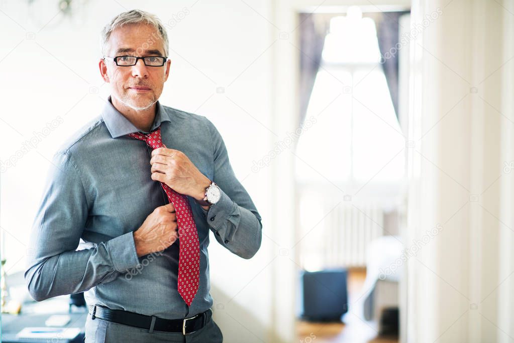 Mature businessman on a business trip standing in a hotel room, getting dressed.