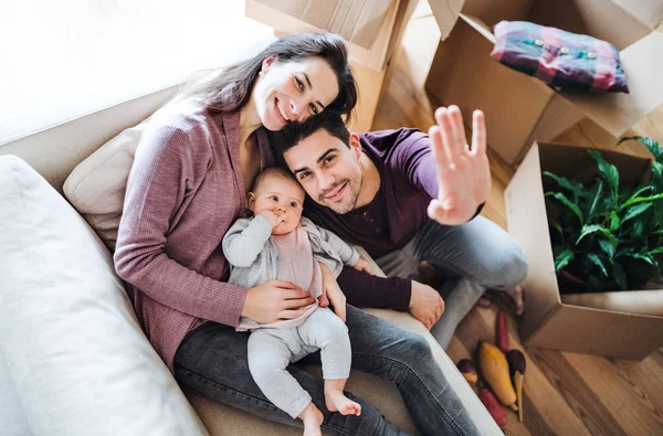 Um retrato de um jovem casal com um bebê e caixas de papelão se movendo em uma nova casa . — Fotografia de Stock