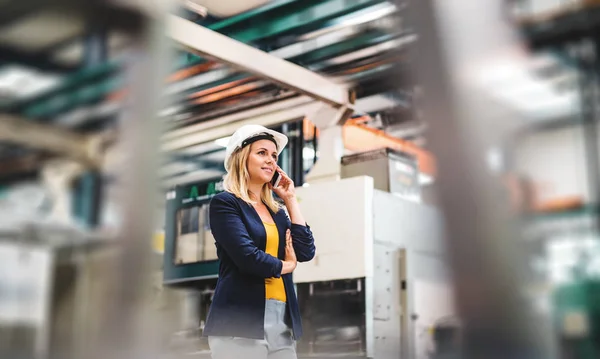 A portrait of an industrial woman engineer on the phone, standing in a factory. — Stock Photo, Image