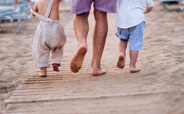 Uma parte central do pai com duas crianças pequenas andando na praia de areia de férias . — Fotografia de Stock