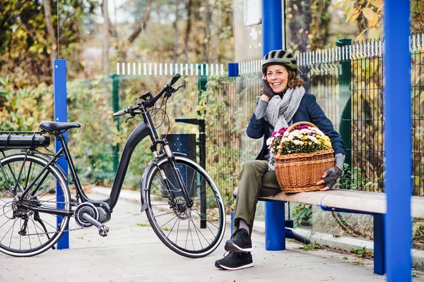 Electrobike と花の町で屋外のベンチに座っている年配の女性. — ストック写真