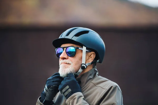 Активный пожилой человек стоит на улице в городе, надевает велосипедный шлем . — стоковое фото