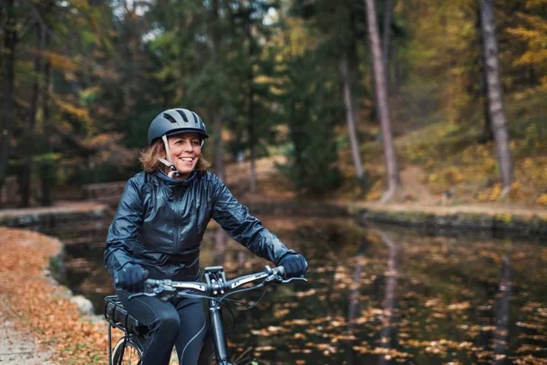 Seniorin mit Elektrofahrrad im Herbst auf Straße im Park unterwegs. — Stockfoto