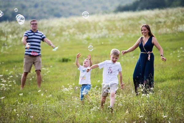 Une jeune famille avec deux petits fils marchant dans la nature, soufflant des bulles de savon . — Photo