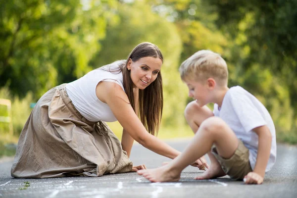 Un petit garçon avec sa mère dessinant de la marelle sur une route dans un parc un jour d'été . — Photo