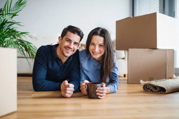 Una pareja joven con una taza y cajas de cartón moviéndose en un nuevo hogar . — Foto de Stock