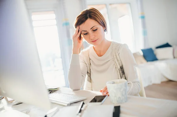 Une jeune femme fatiguée à l'intérieur, travaillant dans un bureau à domicile . — Photo