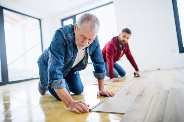 Ein reifer Mann mit seinem älteren Vater, der Vinylböden verlegt, ein neues Wohnkonzept. — Stockfoto