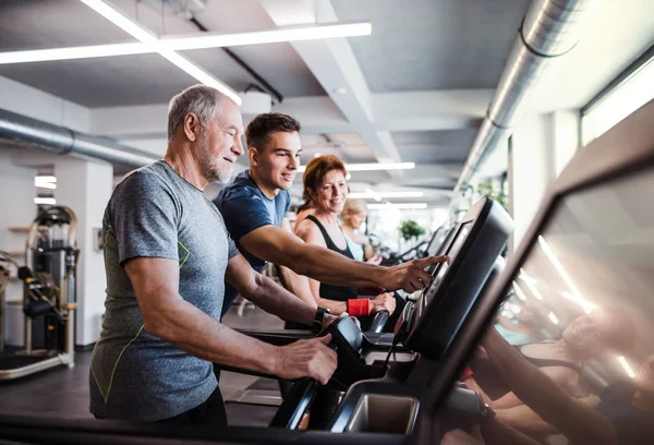 Un groupe de personnes âgées en salle de gym avec un jeune entraîneur qui fait de l'exercice cardio . — Photo