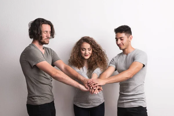 Retrato de jovem alegre com dois meninos amigos de pé em um estúdio, mãos empilhadas . — Fotografia de Stock