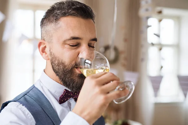 Um retrato de homem maduro dentro de casa em um conjunto de quarto para uma festa, beber vinho . — Fotografia de Stock