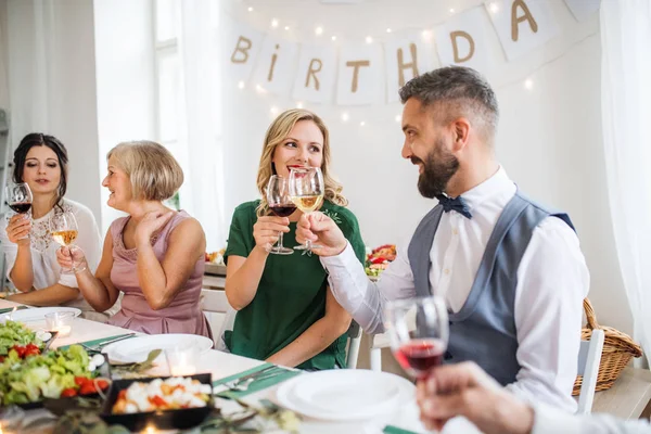 Een grote familie zittend aan een tafel op een indoor verjaardagsfeestje, rammelende bril. — Stockfoto