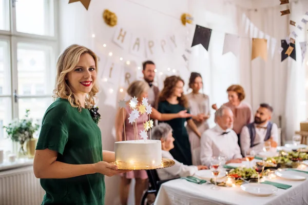 Uma jovem segurando um bolo de aniversário em uma festa indoor . — Fotografia de Stock