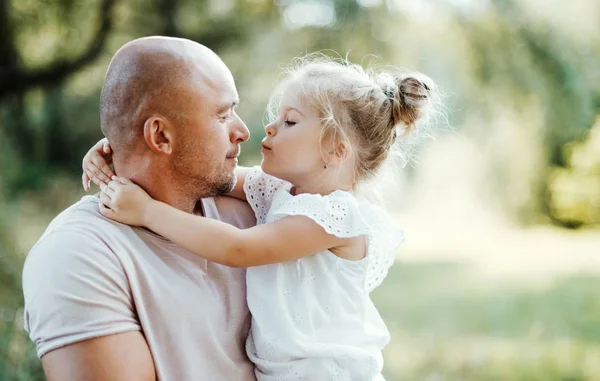 Jovem pai na natureza segurando pequena filha nos braços . — Fotografia de Stock