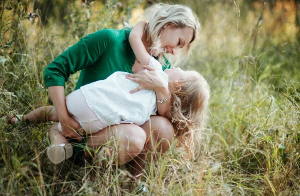 Young mother in nature holding small daughter in summer.
