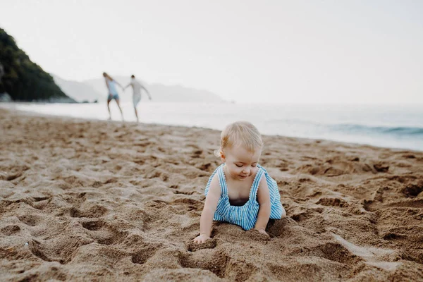 Seorang gadis balita kecil bermain di pasir di pantai pada liburan musim panas . — Stok Foto