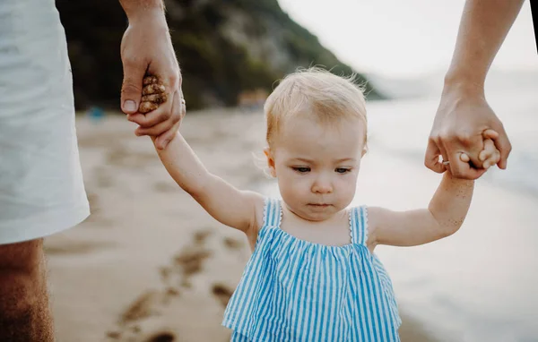 Una sección media de padres con hija pequeña caminando en la playa en las vacaciones de verano . —  Fotos de Stock