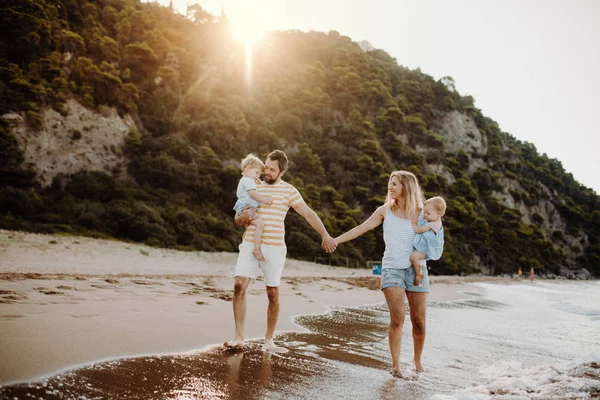 Una familia con dos niños pequeños caminando en la playa en vacaciones de verano al atardecer . — Foto de Stock