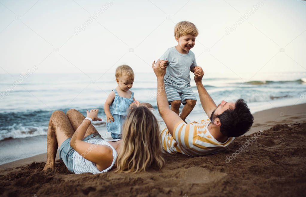 A family with two toddler children lying on sand beach on summer holiday.