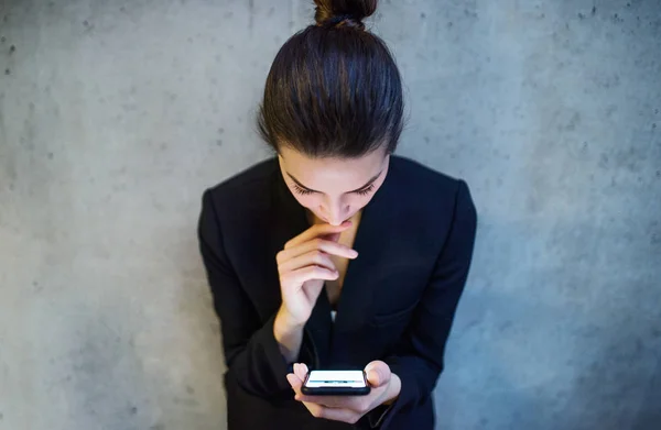 Una vista dall'alto della giovane donna d'affari con smartphone in piedi contro il muro di cemento in ufficio . — Foto Stock