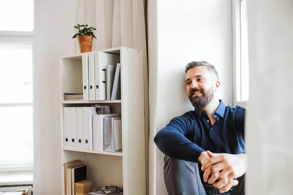 Homme d'affaires mature hipster assis sur un rebord de fenêtre dans un bureau moderne . — Photo