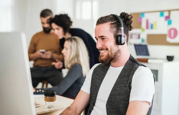 Jovem empresário com fones de ouvido e colegas em um escritório moderno . — Fotografia de Stock