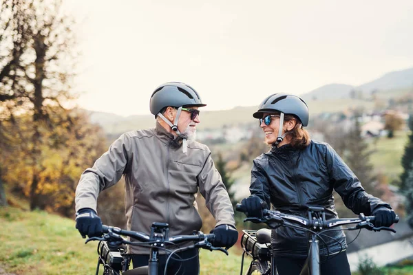 Aktivt seniorpar med elektrocykler stående udendørs på en vej i naturen . - Stock-foto