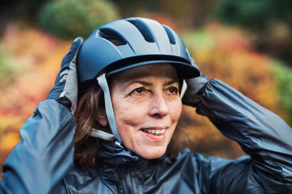 A close-up of active senior woman standing outdoors, putting on bicycle helmet.