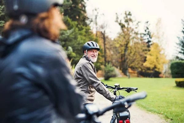 Active senior couple with electrobikes standing outdoors on a road in nature. — Stock Photo, Image
