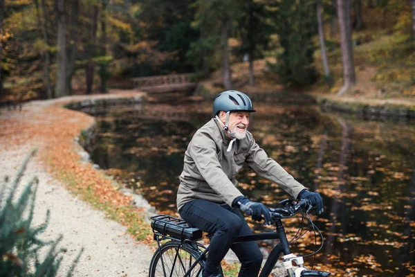 Un hombre mayor con bicicleta eléctrica al aire libre en una carretera en el parque en otoño . —  Fotos de Stock