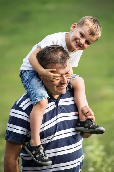 Ojciec, dając piggyback jazdy na małym synem w przyrodzie w letni dzień. — Zdjęcie stockowe