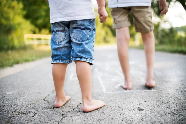 En bakre vy av två små pojkar hopscotching på en väg i parken på en sommardag. — Stockfoto