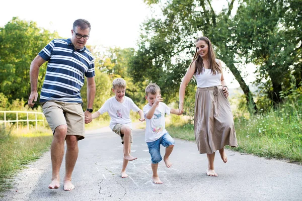 Eine Familie mit zwei kleinen Söhnen, die an einem Sommertag barfuß auf einer Straße im Park hüpft. — Stockfoto