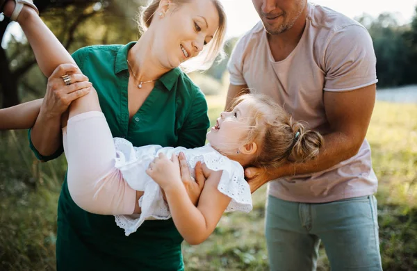 Giovane famiglia con una piccola figlia nella natura estiva soleggiata, divertendosi . — Foto Stock