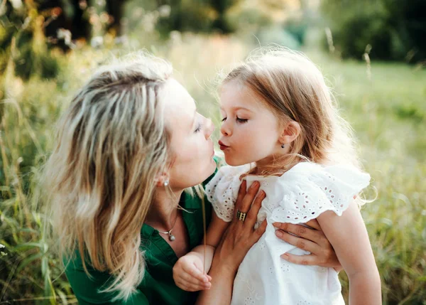 Jovem mãe na natureza com a filha pequena, beijando . — Fotografia de Stock