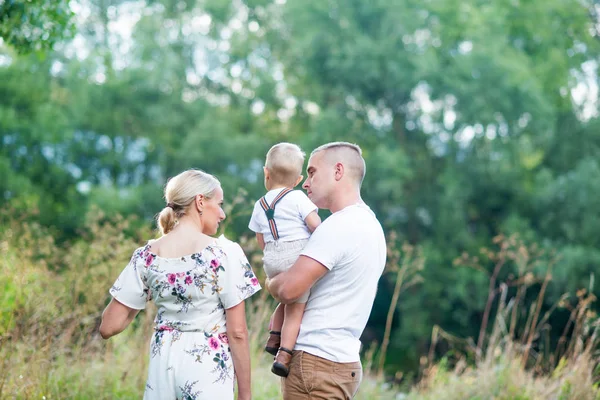 Família jovem com um menino pequeno na natureza ensolarada do verão. Vista traseira . — Fotografia de Stock