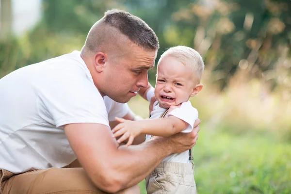 Jovem pai com um pequeno filho criança chorando na natureza ensolarada verão . — Fotografia de Stock