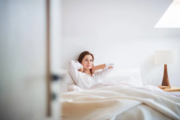 Una joven sentada en la cama en el interior por la mañana en un dormitorio, descansando . —  Fotos de Stock