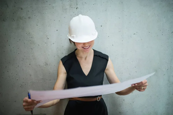 Young businesswoman or architect with a helmet and blueprints standing in office. — Stock Photo, Image