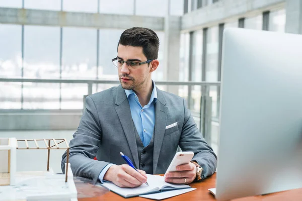 Joven empresario o arquitecto con ordenador y smartphone en oficina, trabajando . — Foto de Stock