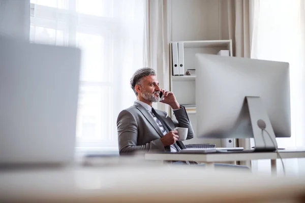 Affärsman med smartphone, kaffe och dator sitter vid bordet, att ringa ett telefonsamtal. — Stockfoto