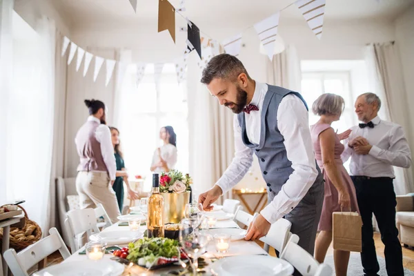 Ein reifer Mann mit Schleife und Weste deckt einen Tisch für eine Indoor-Party. — Stockfoto