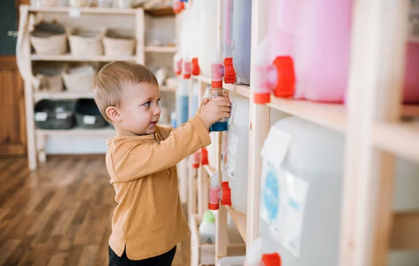 Un pequeño niño de pie junto a los dispensadores en el taller de residuos cero . — Foto de Stock