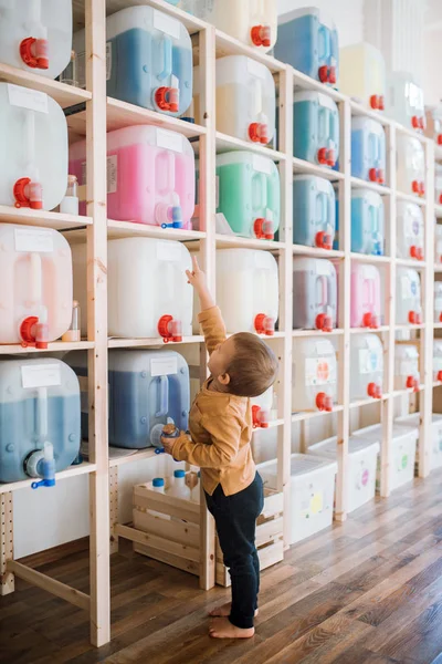 Un pequeño niño de pie junto a los dispensadores en el taller de residuos cero . — Foto de Stock