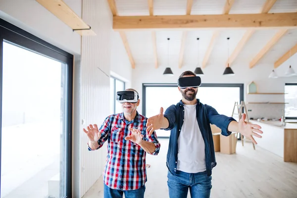 Um homem com óculos de realidade virtual e seu pai sênior fornecendo casa nova, um novo conceito de casa . — Fotografia de Stock
