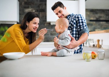 Evde Genç bir aile onu besleyen bir kadın ve bir bebek tutan bir adam.
