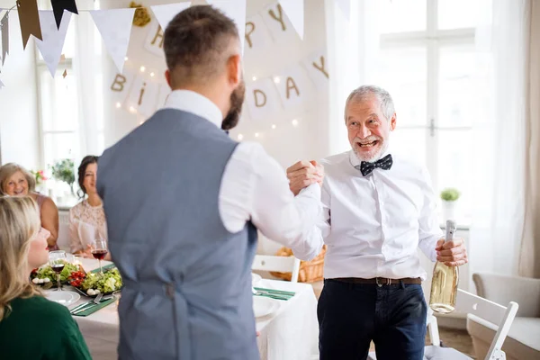 Een man een fles wijn geven zijn vader op indoor verjaardagsfeestje, een viering concept. — Stockfoto