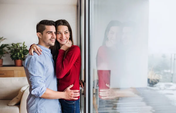 Ungt par i kärlek stående genom fönstret hemma, kramas. Kopiera utrymme. — Stockfoto