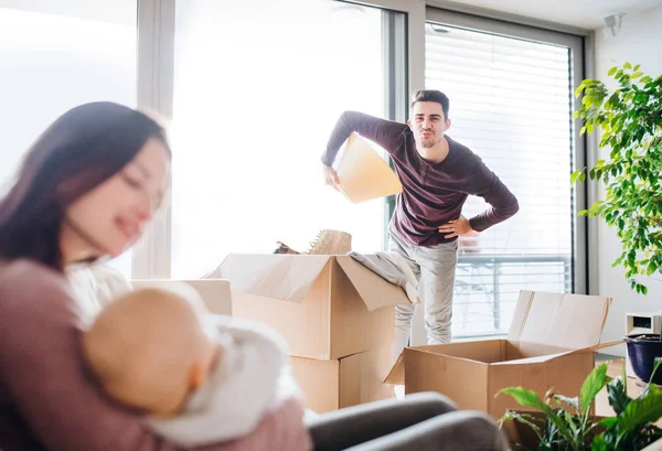 Um retrato de um jovem casal com um bebê e caixas de papelão se movendo em uma nova casa . — Fotografia de Stock
