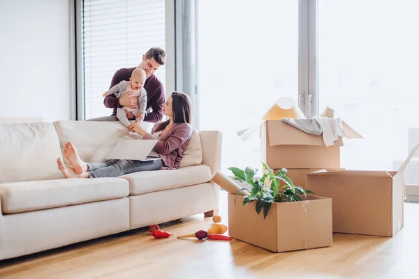 Portrait d'un jeune couple avec un bébé et des boîtes en carton emménageant dans une nouvelle maison . — Photo